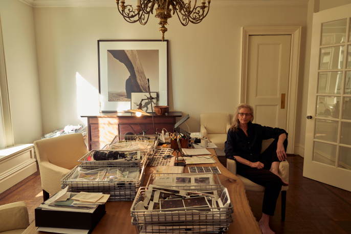 Annie Leibovitz sitting by her desk filled photos and magazines.