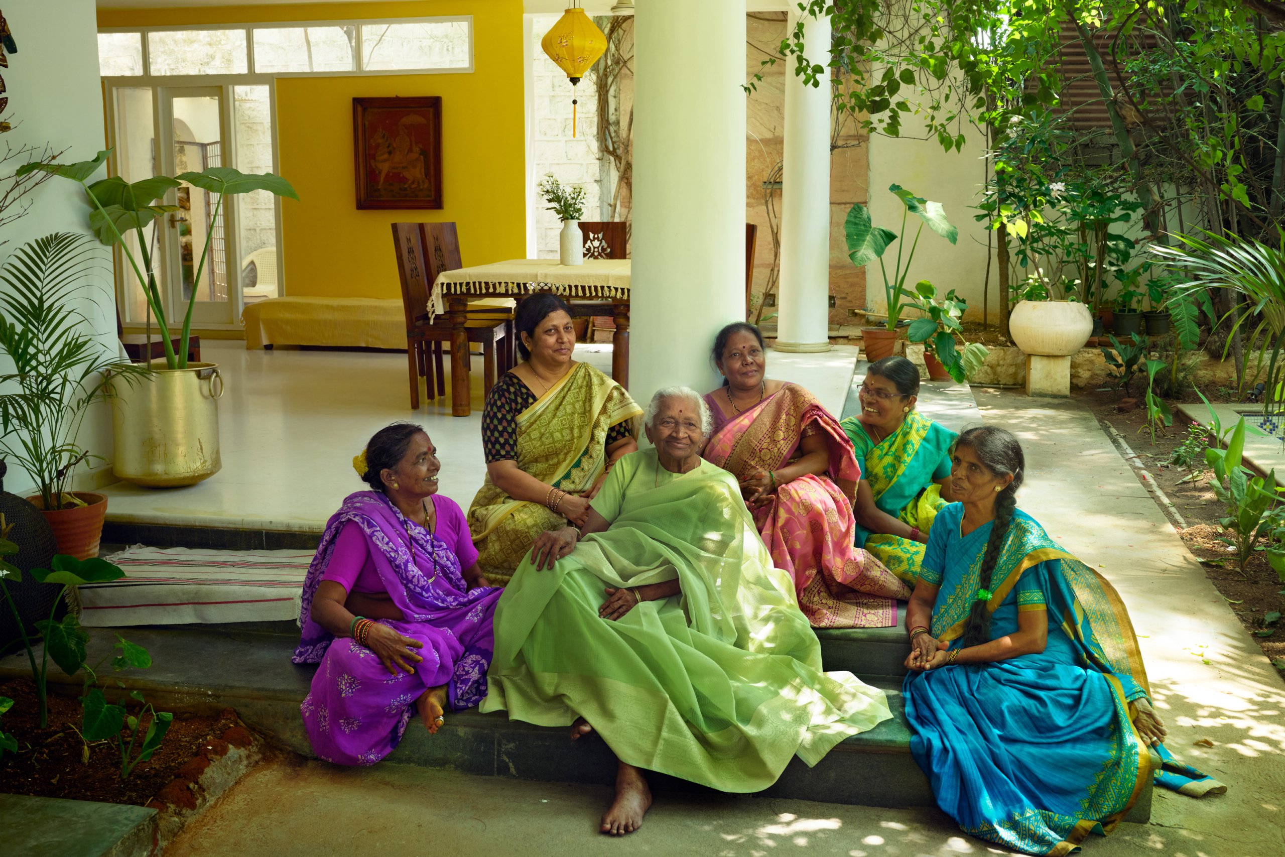 Revathi sitting on her patio surrounded by a group of friends smiling.