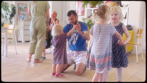 Children and adults dancing together in the common area of their collective house.