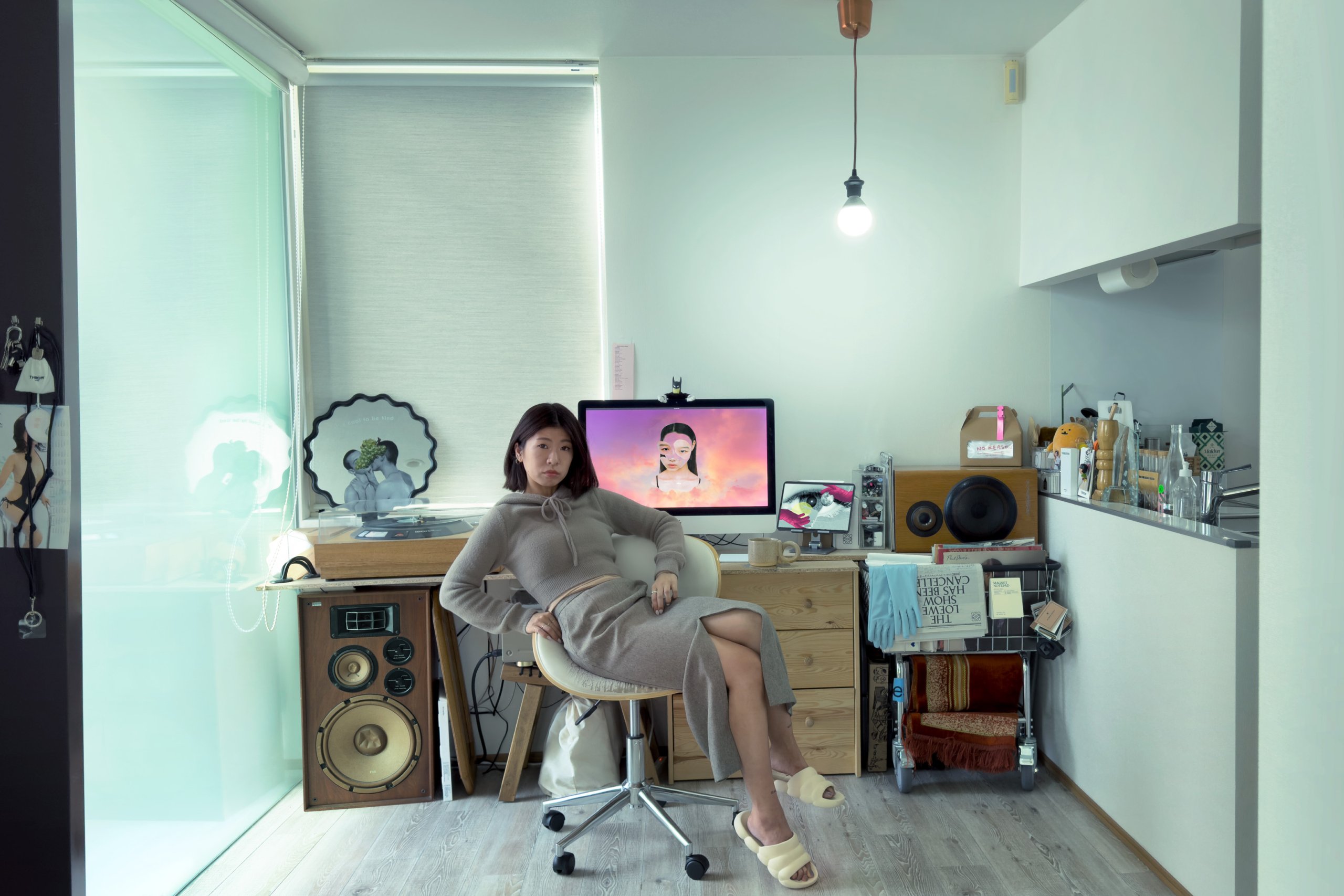 Manami sitting on a chair in front of her large desk where she has her computer, vinyl player and large speakers.