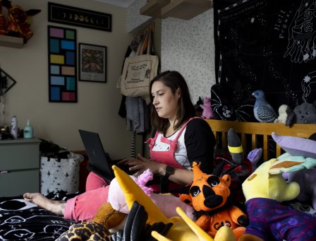 Lady sitting on her bed, using her laptop, surrounded by plush toys