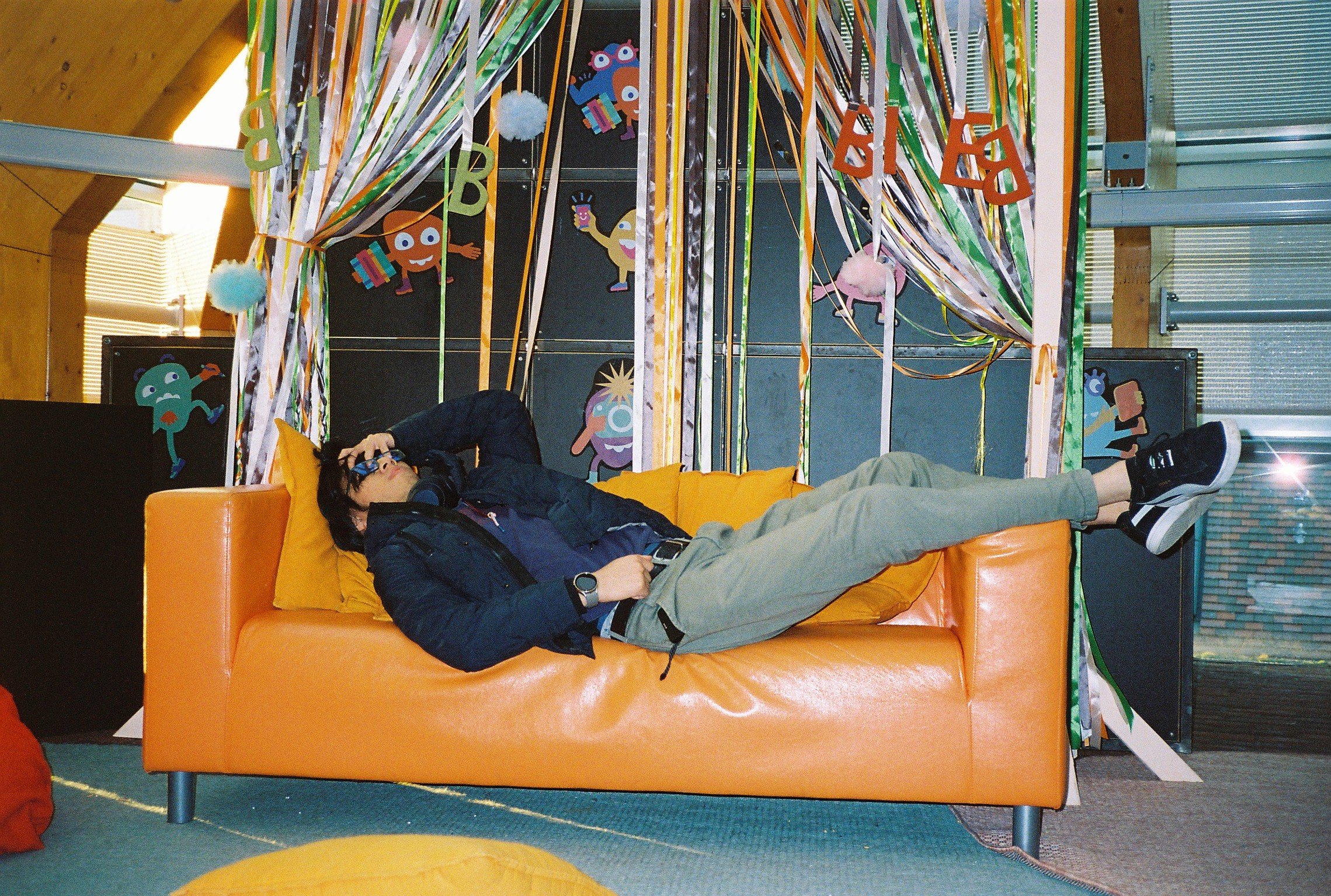 Trams brother laying in an orange sofa in front of colorful party decorations.