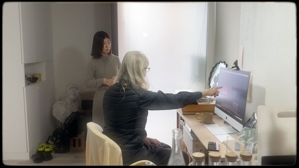 Annie pointing to Manamis computer screen while Manami is standing next to her.