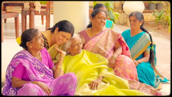 Revathi sitting outside on the terrace surrounded by her five caretakers all dressed in colorful saris.