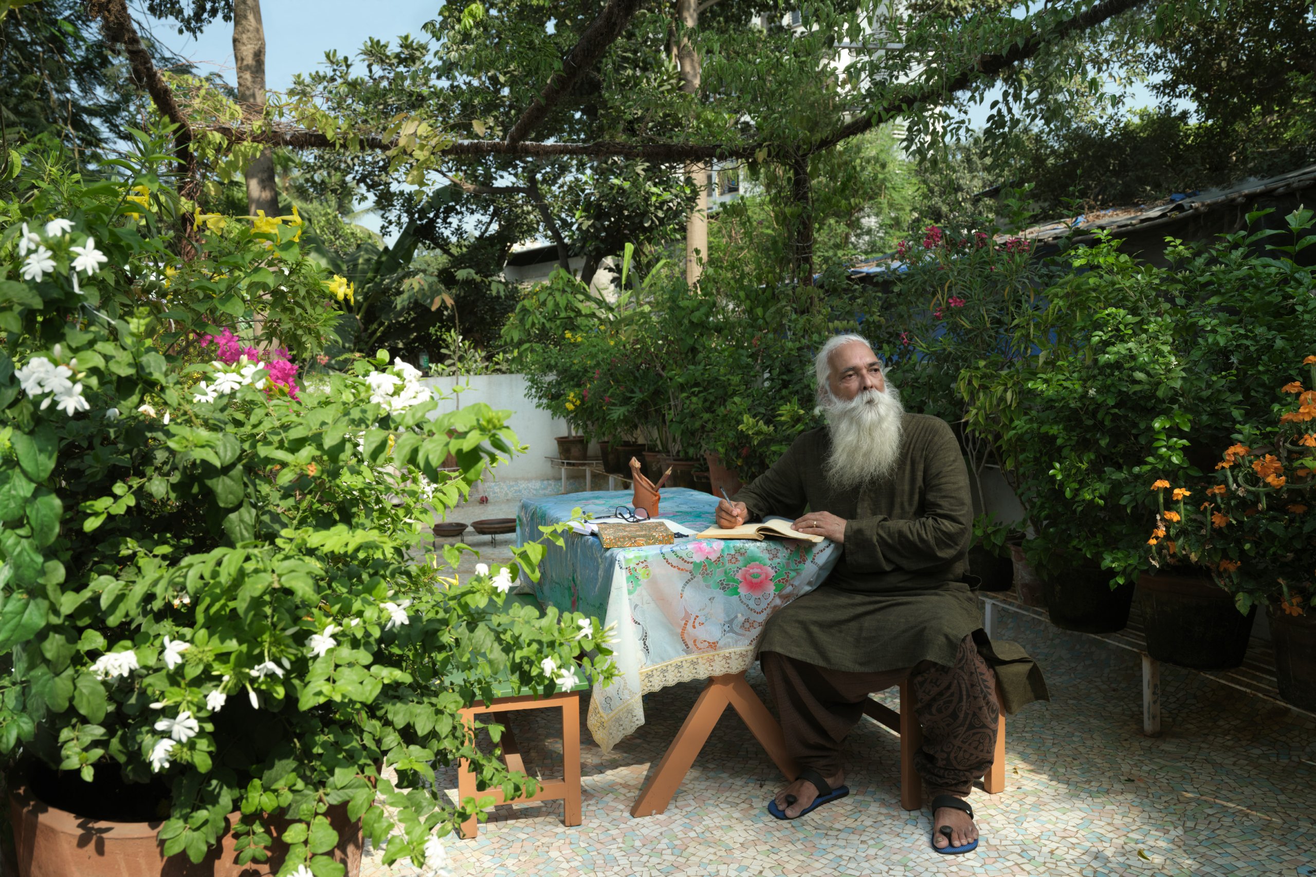 Gangadharan sitting by a clothed table in his garden, surrounded by flower and plants.