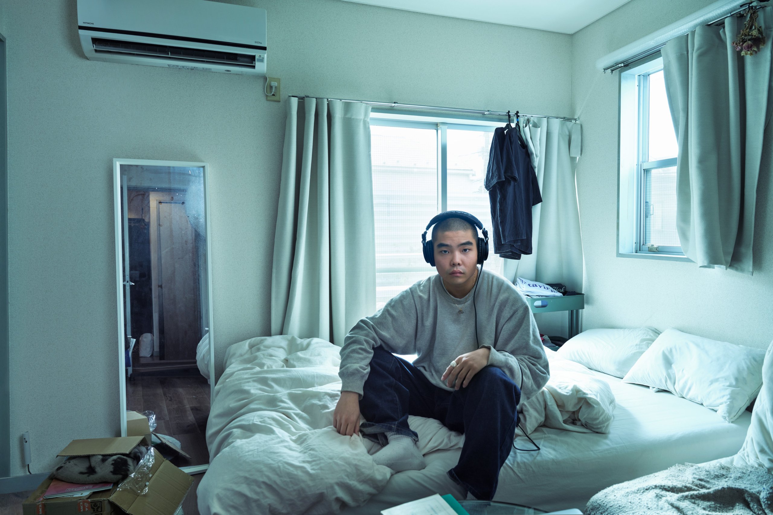 Sota sitting on his bed wearing headphones.