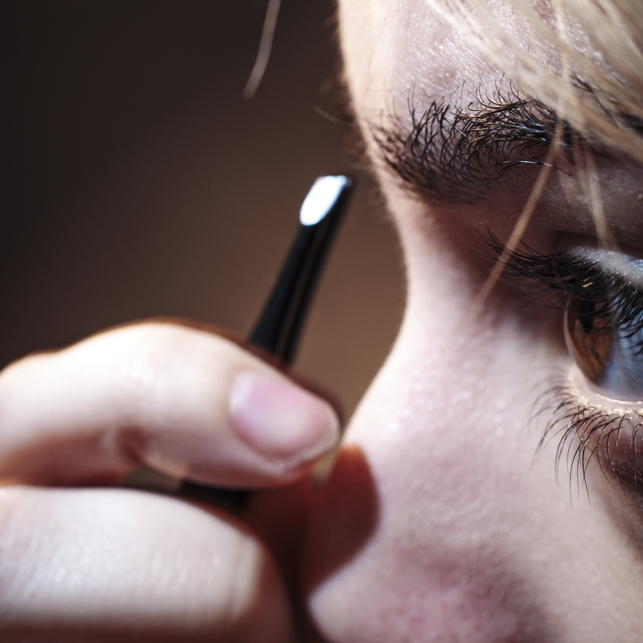 Closeup of Tomas girlfriend plucking her eyebrows with tweezers.