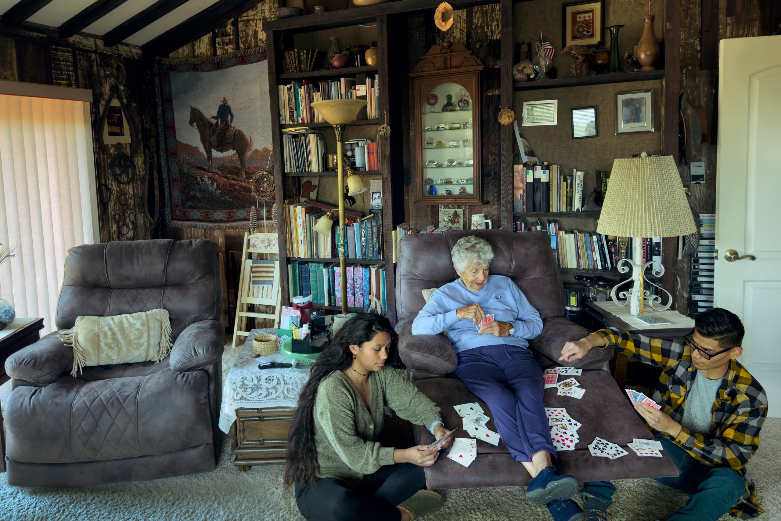 Raul sitting in the livingroom with his fiancé and grandmother playing cards.